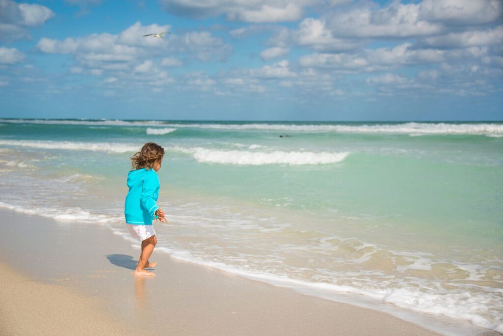 enfant jouant au bord d’une eau turquoise, sur une plage calme